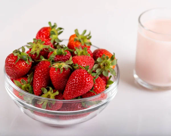 Fresh strawberries in a glass bowl and a glass of strawberry milk