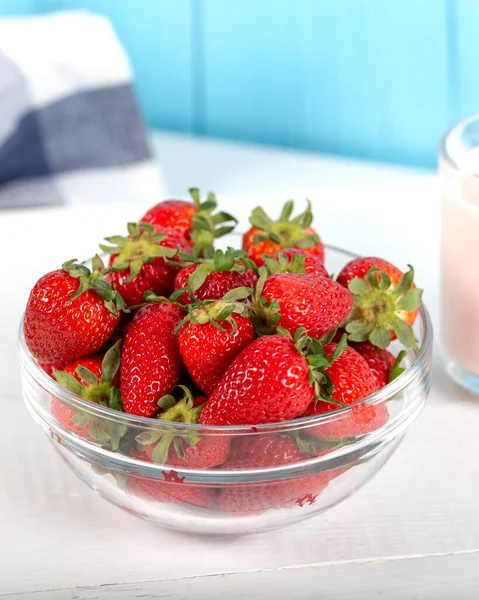 Fresh strawberries in a glass bowl and a glass of strawberry milk