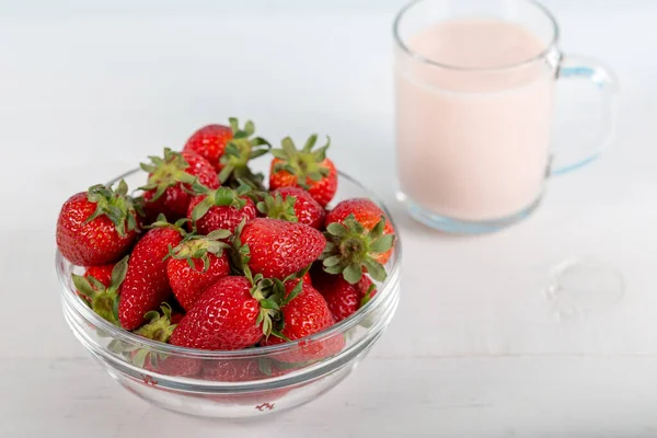 Fresh strawberries in a glass bowl and a glass of strawberry milk