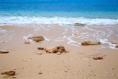 Turkuaz renkli deniz ve taşlar kumsalda.