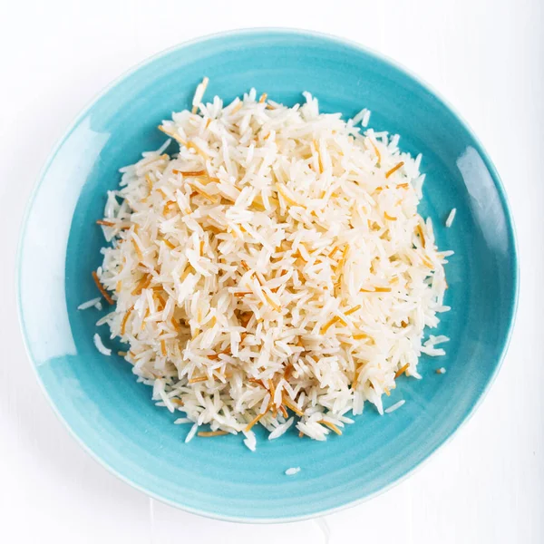 Beyaz arka planda seramik bir kase veya tabakta servis edilen pişmiş basmati pilavının üst görüntüsü.