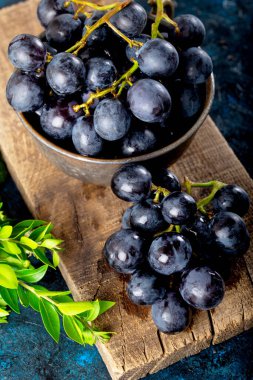 Taze siyah üzümler ve yapraklar koyu taştan arka planda kırsal bir kereste üzerinde.