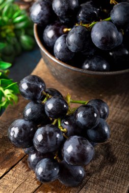 Taze siyah üzümler ve yapraklar koyu taştan arka planda kırsal bir kereste üzerinde.