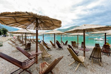 Boş kumsal. Plaj ahşap mobilyaları, şemsiyeler. Kötü bir gün. Karadağ, Kotor Körfezi