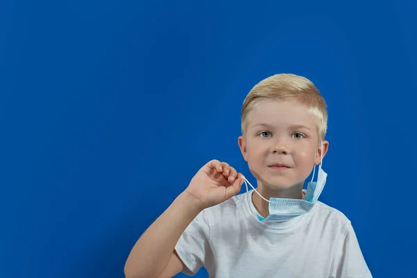 Європейський хлопчик знімає маску на синьому фоні. — стокове фото