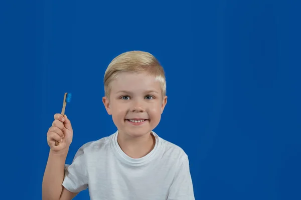 Criança segura uma escova de dentes em um fundo azul liso — Fotografia de Stock