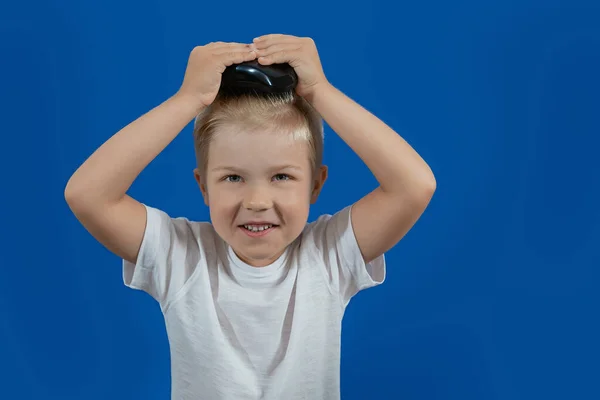 Маленький хлопчик чистить волосся гребінцем на синьому фоні — стокове фото