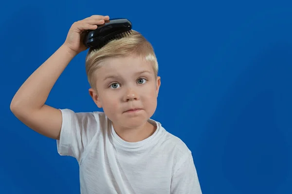 Маленька дитина розчісує волосся на синьому фоні — стокове фото