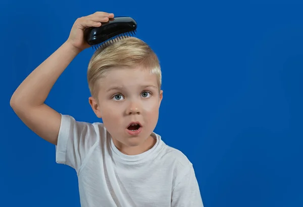 A criança independentemente penteia o seu cabelo e surpreende-se no contexto blu — Fotografia de Stock