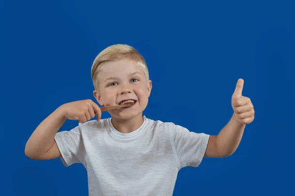 Criança escovando seus dentes em um fundo azul liso — Fotografia de Stock