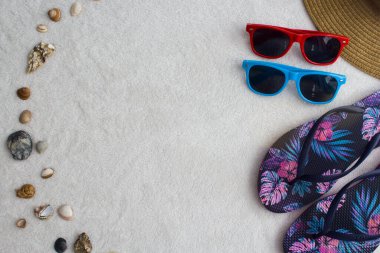 Plaj eşyaları, hasır şapka, mavi ve pembe desenli terlikler, kırmızı ve mavi güneş gözlükleri, deniz salyangozları ve metin için yer.