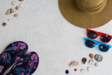 Plaj eşyaları, hasır şapka, mavi ve pembe desenli terlikler, kırmızı ve mavi güneş gözlükleri, deniz salyangozları ve metin için yer.