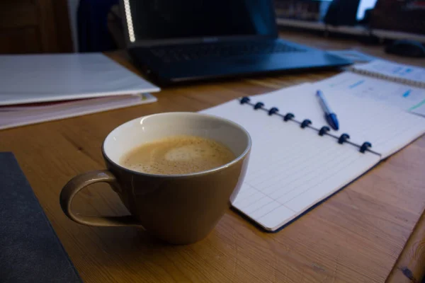 Wooden table, laptop, coffee and notebook with blue pen; study, work from home online.