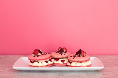 Krema ve çilekle doldurulmuş pembe badem kurabiyeleri. Pastel renkler, pembe arkaplan
