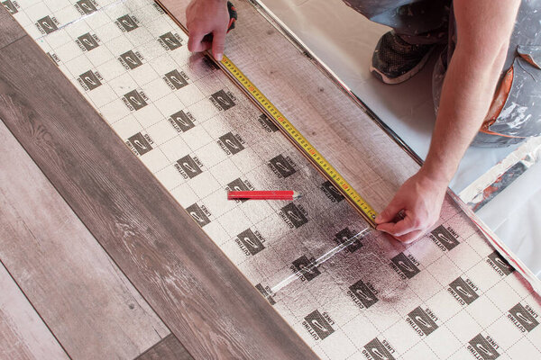 laying a floating floor, including sound insulation, man measures the distance by the meter