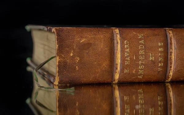 Aynadaki eski bir kitap, deri kaplı, siyah bir arka planı var.