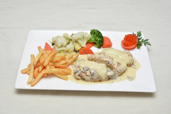 Tavuk cordon bleu, patates kızartması ve sebze salatası. Beyaz tabakta servis ediliyor.