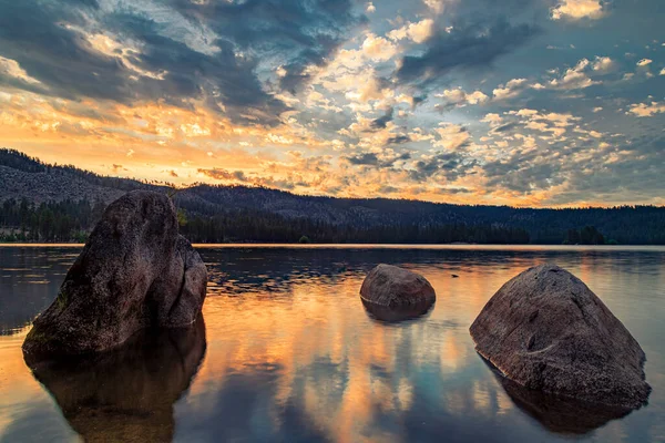 Plumas County, Kuzey Kaliforniya 'da Antelope Gölü' nde gün doğumu ve karamsar bulutlar, büyük kayalar ve sıcak yansımalar içerir..