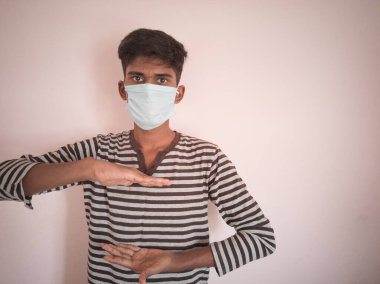 Hintli yakışıklı adam tıbbi maske takıyor ve pembe arka planda ürünleri gösteren tişört giyiyor..