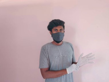 Koronavirüsten korumak için maske ve eldiven takan Güney Asyalı bir adam. Corona virüsü salgını. Gri renkli maskeli ve beyaz eldivenli biri. Pembe arka planda izole edilmiş.