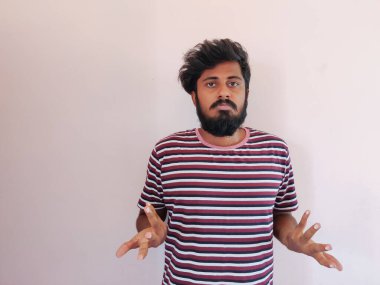 Üzgün Hintli sakallı adam, elleri ve kollarıyla çaresiz bir hareket sergiliyor, ağzı sanki ne yapacağını bilmiyormuş gibi kıvrılmış. Beyaz arka planda izole edilmiş. Soyunmuş tişört