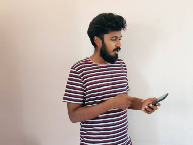 Hintli sakallı adam cep telefonuna bakıyor ve tepki veriyor. Adam soyulmuş tişört giymiş. Beyaz arkaplanda izole.