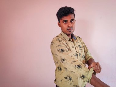 Güney Hintli yakışıklı adam gömleğinin kolunu pembe arka planda katlıyor. Tıraş olmuşsun. Gün ışığı.