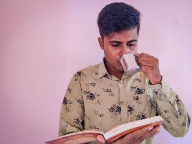 Güney Hintli yakışıklı adam elinde kitap ve kupa tutuyor. Kahve içerken ciddi ciddi kitap okuyorsun. Çeviri:.