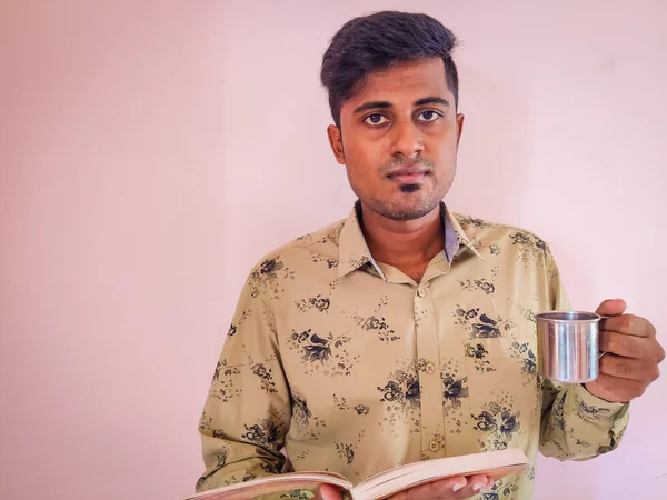 南インドのハンサムな男が本とカップを手に持っている コーヒーを飲みながら本を読む — ストック写真