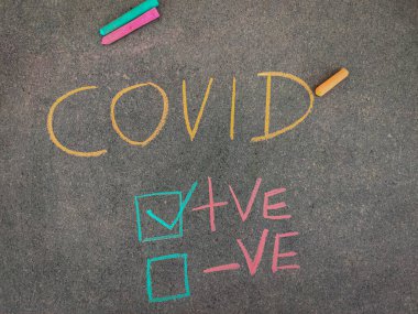 Gri panodaki yazı metni, COVID için pozitif test sonuçlarıyla işaretlenmiş. Renkli tebeşir parçaları kullanılıyor. Corona virüsü konsepti