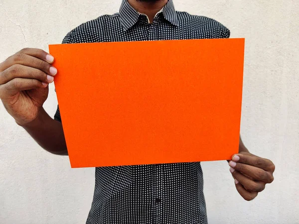 黒シャツの若い男は 空白のオレンジ色のチャートやボードや紙を保持します 白地に隔離された — ストック写真