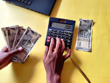 Güney Hintli adam 500 rupi. Hesap makinesi ve dizüstü bilgisayar kullanarak faturalar hesaplanıyor. Sarı arkaplan