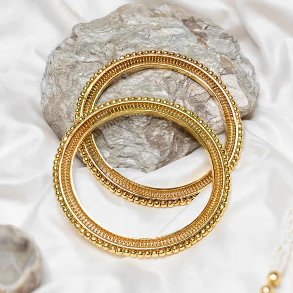 Gold bangles on white silk cloth and stone
