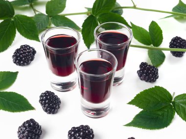 Üç bardak böğürtlen likörü, ayrıca creme de mure olarak da bilinir, beyaz arka planda, böğürtlen filizi ve taze böğürtlenlerle süslenmiş.       