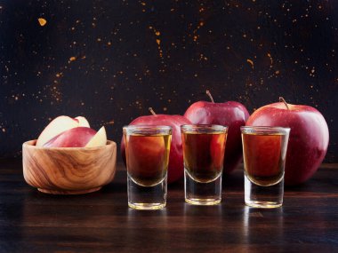 Eskimiş elma brendisi, Calvados ve kırmızı elmalar, koyu kahverengi arka planı olan tahtanın üzerinde.