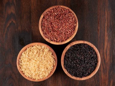 Siyah, kırmızı ve kahverengi pirinçler zeytin ağacından kaselerde, koyu kırsal bir yaban domuzunda.