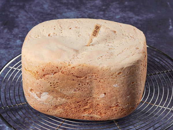 Freshly baked gluten-free bread, made at home with the bread machine, set on a cooling rack, on dark blue background
