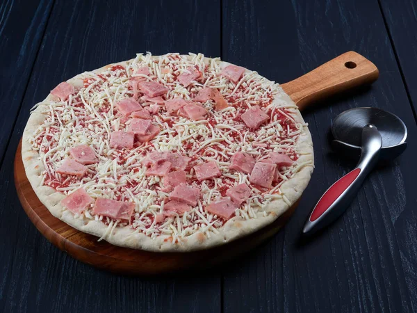 Frozen pizza with ham on a rusty tray, on a dark background