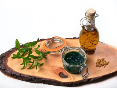 Bir kavanoz taze naneli pesto taze nane yaprağı, çam fıstığı ve bir sürahi zeytinyağı ile ahşap bir tahtaya dizilmiş.