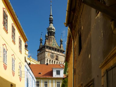 Sighisoara 'daki saat kulesi ortaçağ kalesinin renkli evleriyle dolu bir sokaktan görüldüğü gibi.
