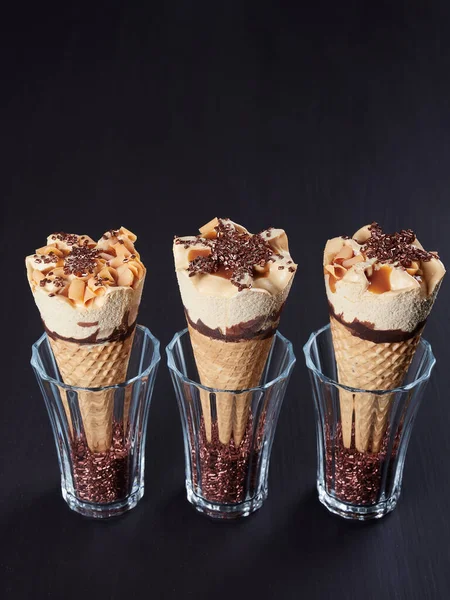 Three caramel ice cream cones, set in glasses filled with sugar crystals, on dark brown background