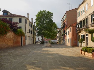 Evleri, eski ortaçağ kuyusu başları ve yapraklı yeşil ağaçları olan açık konut meydanı, Venedik, Veneto, İtalya