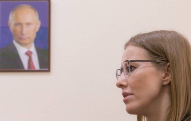 Duvardaki Vladimir Putin portresinin arka planında Kseniya Sobchak Rus TV sunucusu, gazeteci, sosyete ve aktris. Rusya 'nın başkan adayı.