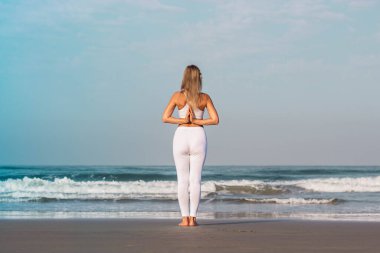 Beyaz elbiseli kız sahilde duruyor ve yoga ve meditasyon yapıyor.