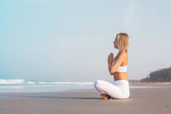 Una hermosa chica en ropa blanca está sentada en el océano y practicando yoga y meditación — Foto de Stock