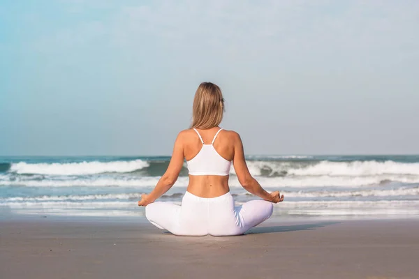 Uma menina bonita em roupas brancas está sentado no oceano e praticando ioga e meditação — Fotografia de Stock