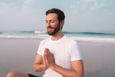 Adam deniz kıyısında lotus pozisyonunda oturur ve meditasyon yapar..