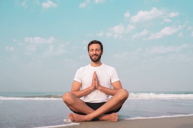 Adam deniz kıyısında lotus pozisyonunda oturur ve meditasyon yapar..