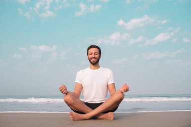 Adam deniz kıyısında lotus pozisyonunda oturur ve meditasyon yapar..