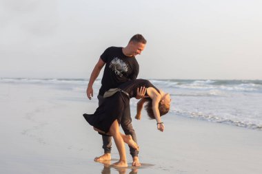 Gün batımında terk edilmiş tropik bir plajda koşan, gülen ve el ele tutuşan mutlu iki genç erkek ve kadın.